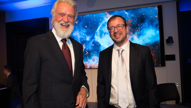 Two men standing together at an event smiling at the camera