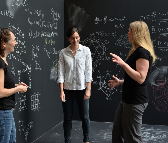 Three women surrounded by chalkboards with equations