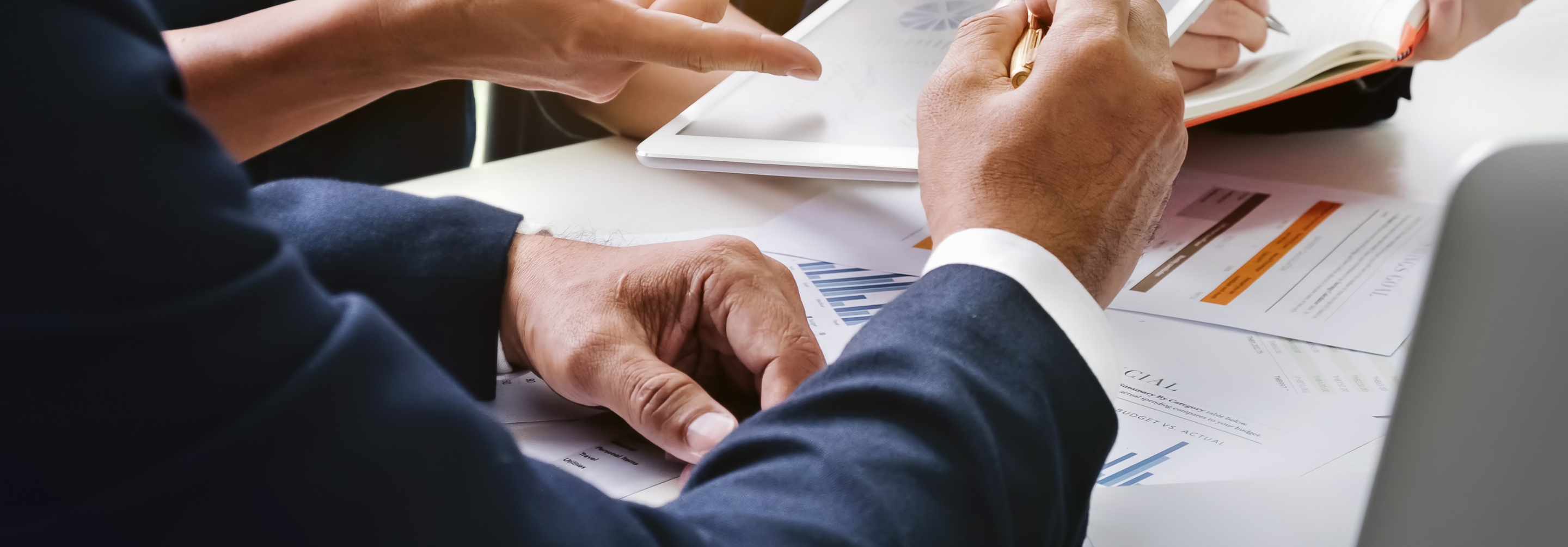 Close up of men and women's hands going over paperwork and a tablet of information